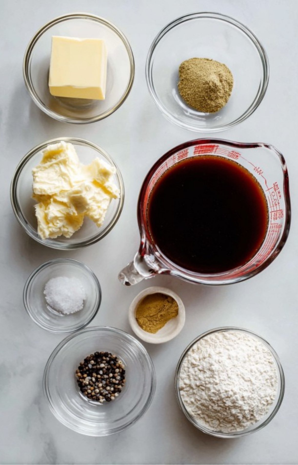 A flatlay of butter, flour, beef stock, salt, pepper, and spices arranged for making homemade beef gravy
