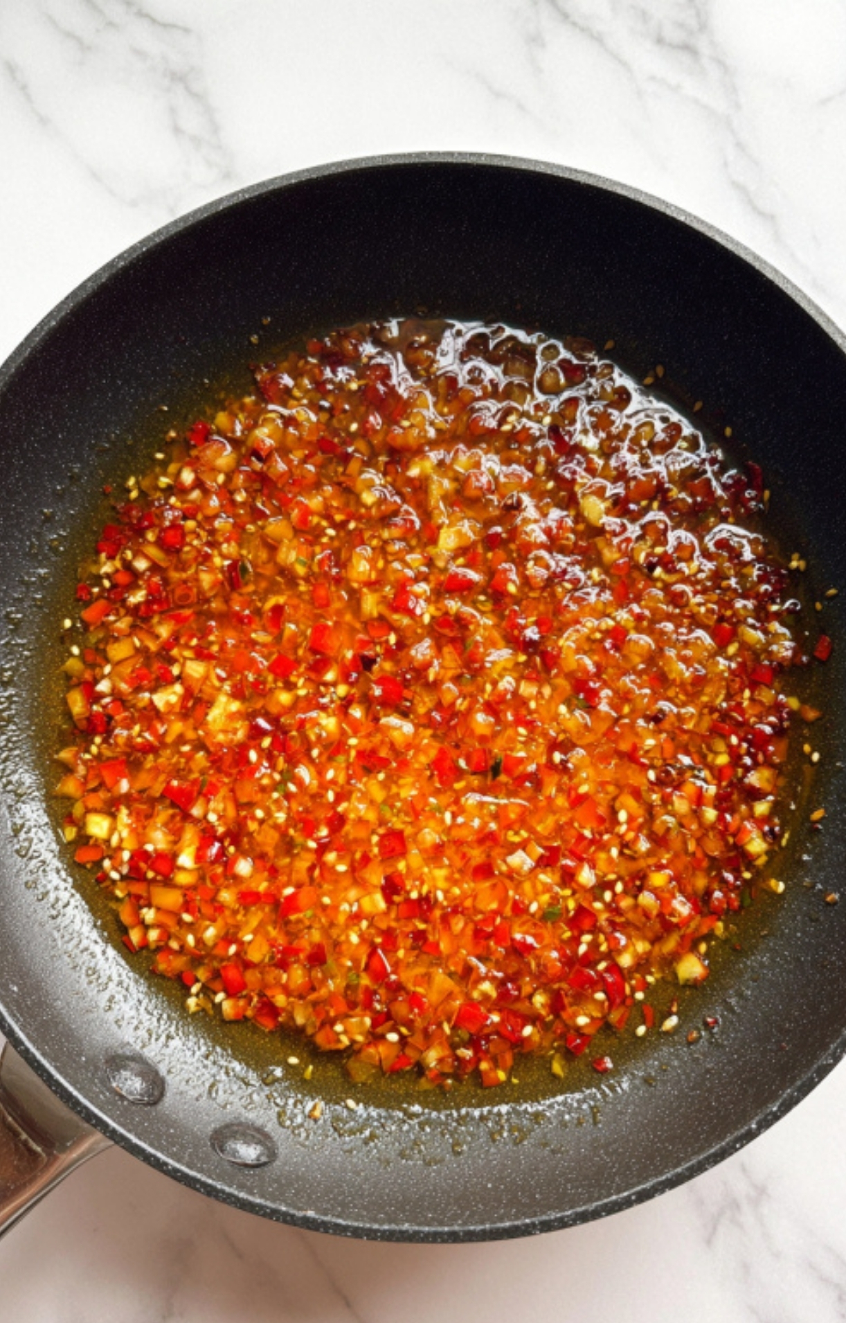 Homemade Asian chili sauce with colorful diced chilies and aromatics sizzling in a frying pan.