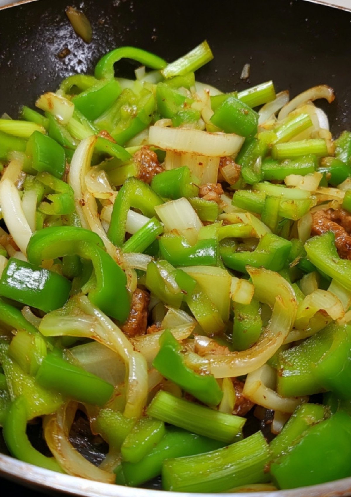 Green bell peppers, onions, and celery being stir-fried in a skillet for sweet and sour pork.