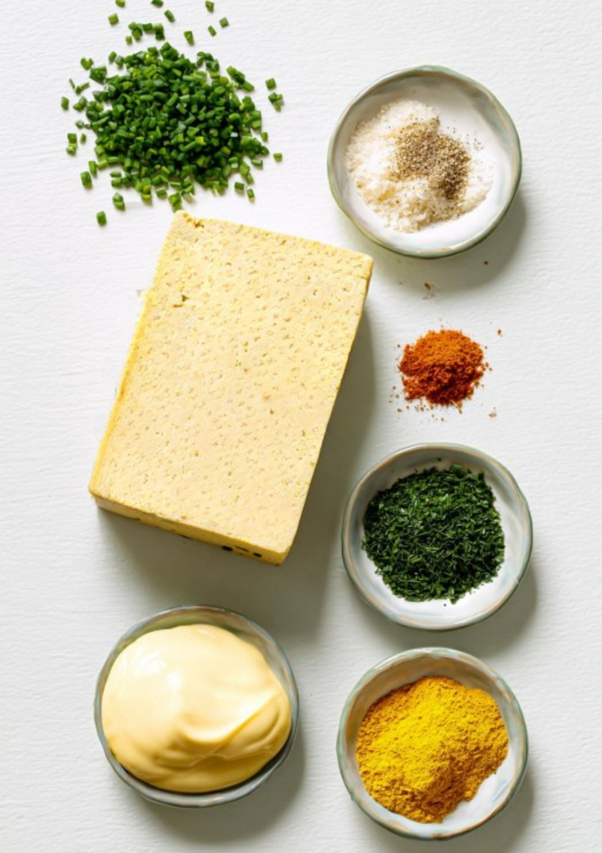 Flat lay of extra-firm tofu, vegan mayo, fresh chives, dill, spices, and nutritional yeast, ready to make tofu egg salad.