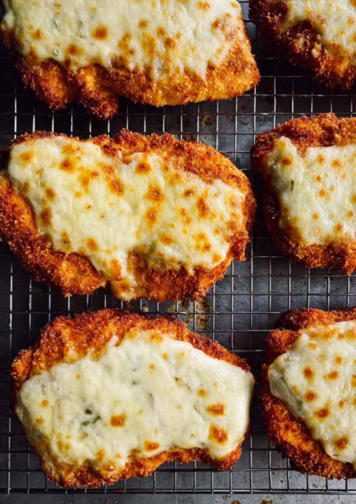 Golden brown breaded chicken cutlets topped with melted mozzarella cheese on a wire rack, ready for sandwiches.