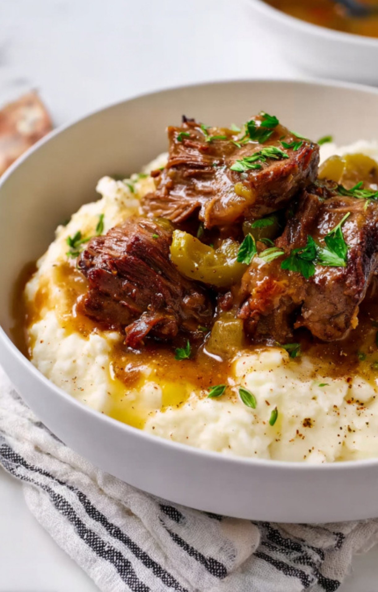 Bowl of creamy mashed potatoes topped with Mississippi Pot Roast, gravy, and fresh herbs, ready to eat.