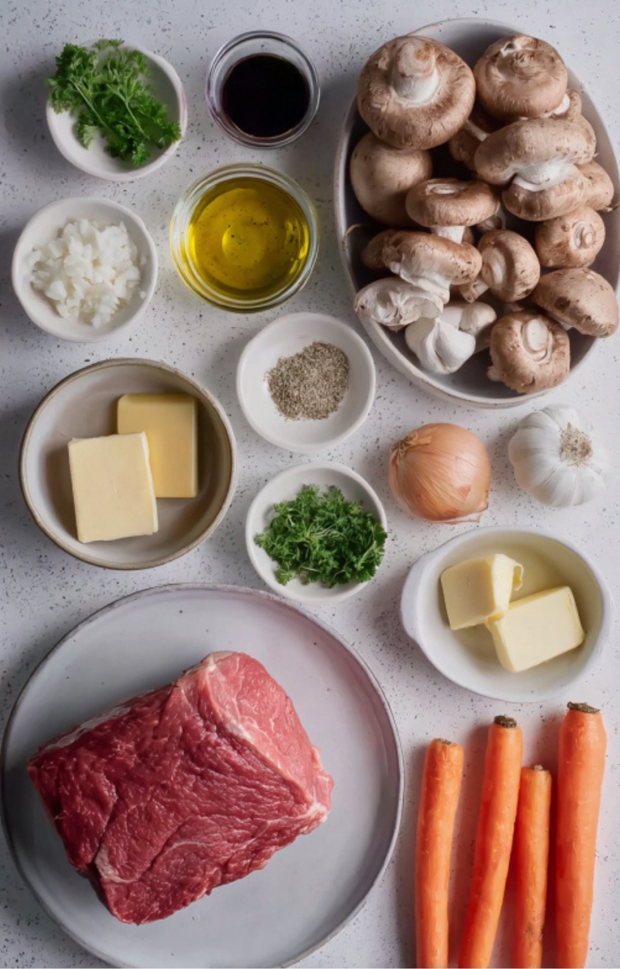 Overhead shot of eye of round roast, carrots, mushrooms, butter, onion, and herbs ready for roasting.