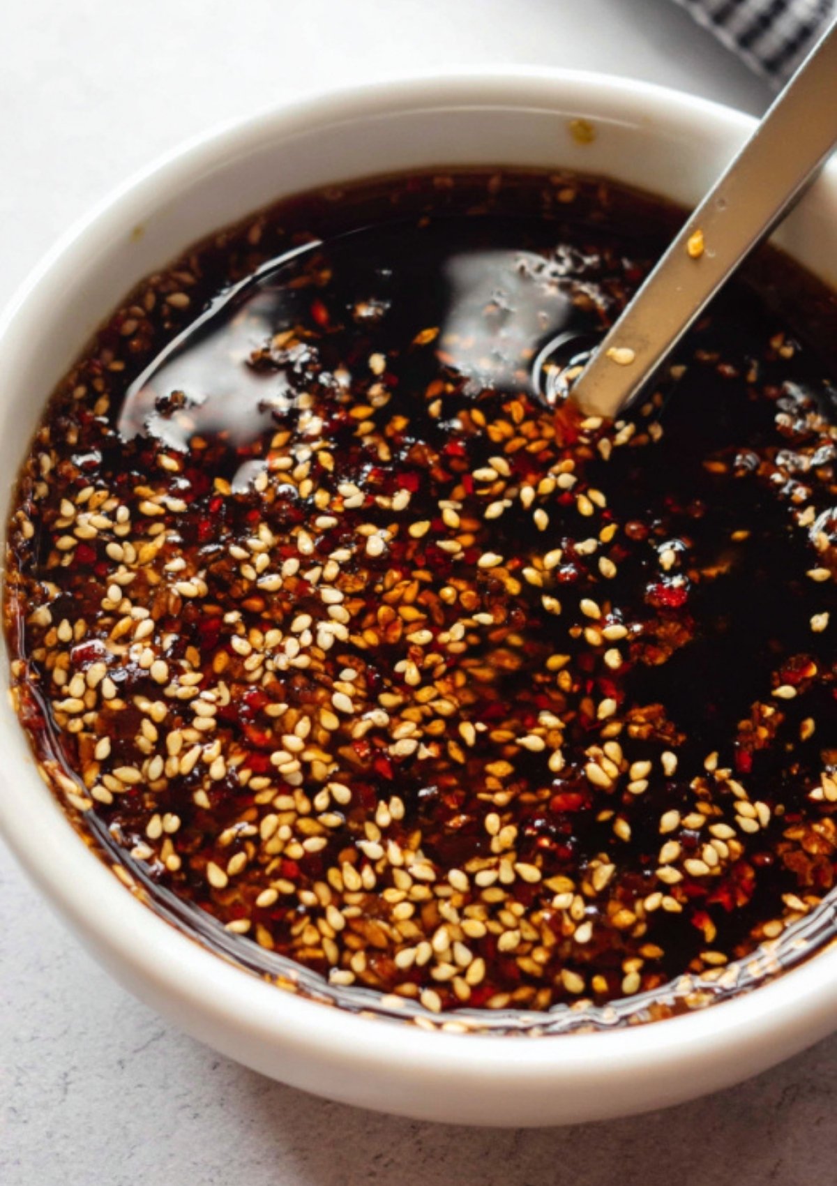 Close-up of homemade garlic sesame sauce with sesame seeds and chili flakes in a white bowl.
