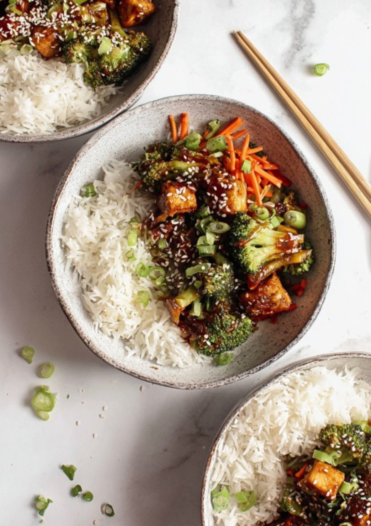 Bowls of fluffy white rice topped with tofu, broccoli, carrots, sesame seeds, and scallions for a colorful, healthy vegan dinner.
