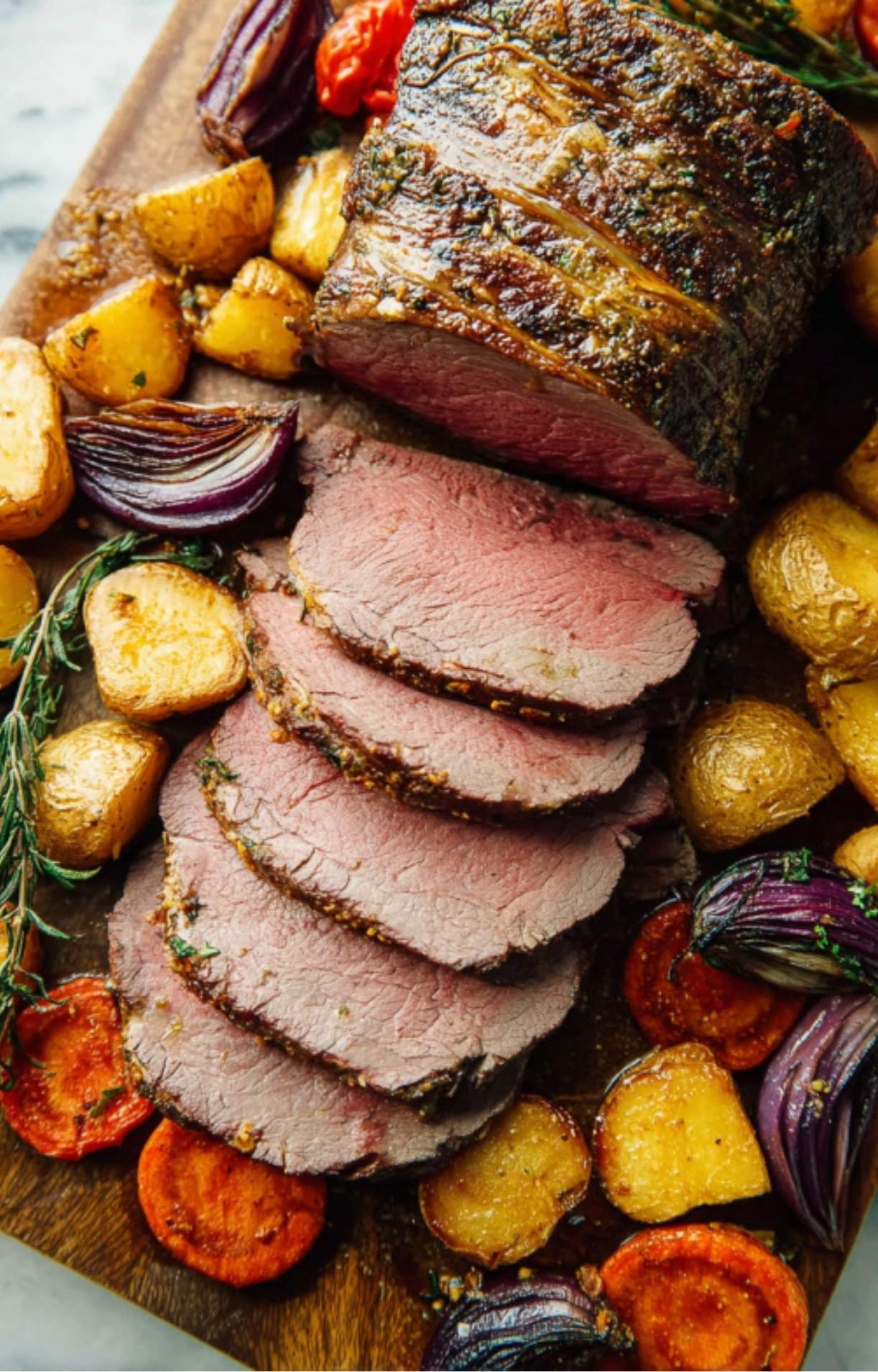 Sliced roast beef with roasted potatoes, carrots, and onions on a wooden board, easy one-pan meal for Sunday roast or holiday entertaining.
