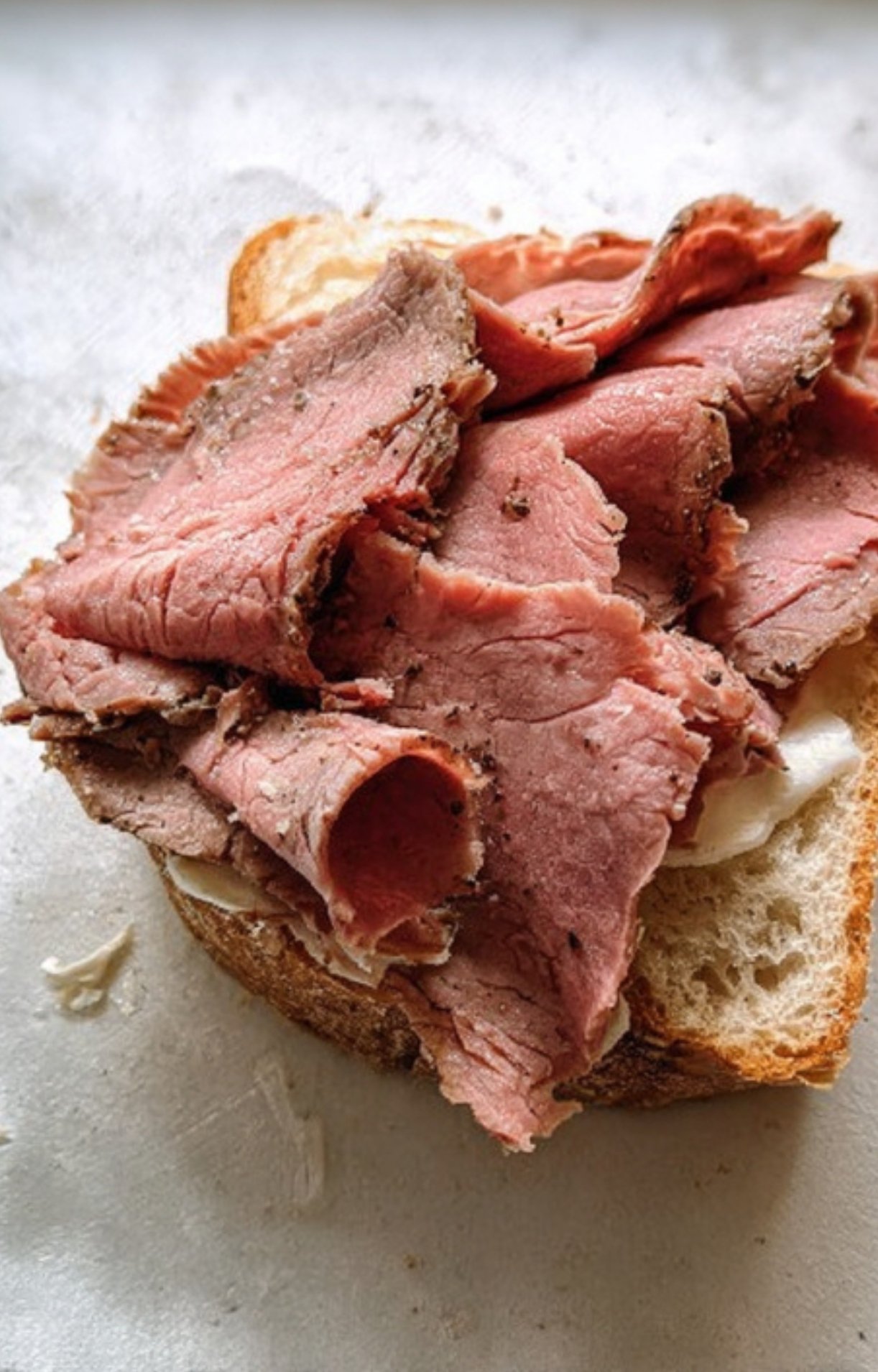 Pile of thinly sliced roast beef layered on fresh sandwich bread for a quick homemade lunch