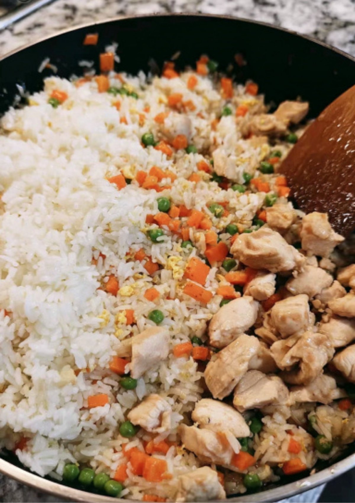 Pan of homemade chicken fried rice with carrots, peas, eggs, and chicken, ready to mix for a quick dinner.