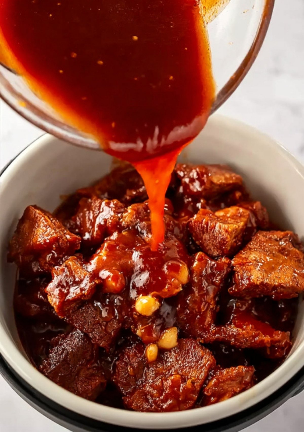 Barbecue sauce being poured over tender pulled pork in a bowl for bold flavor.