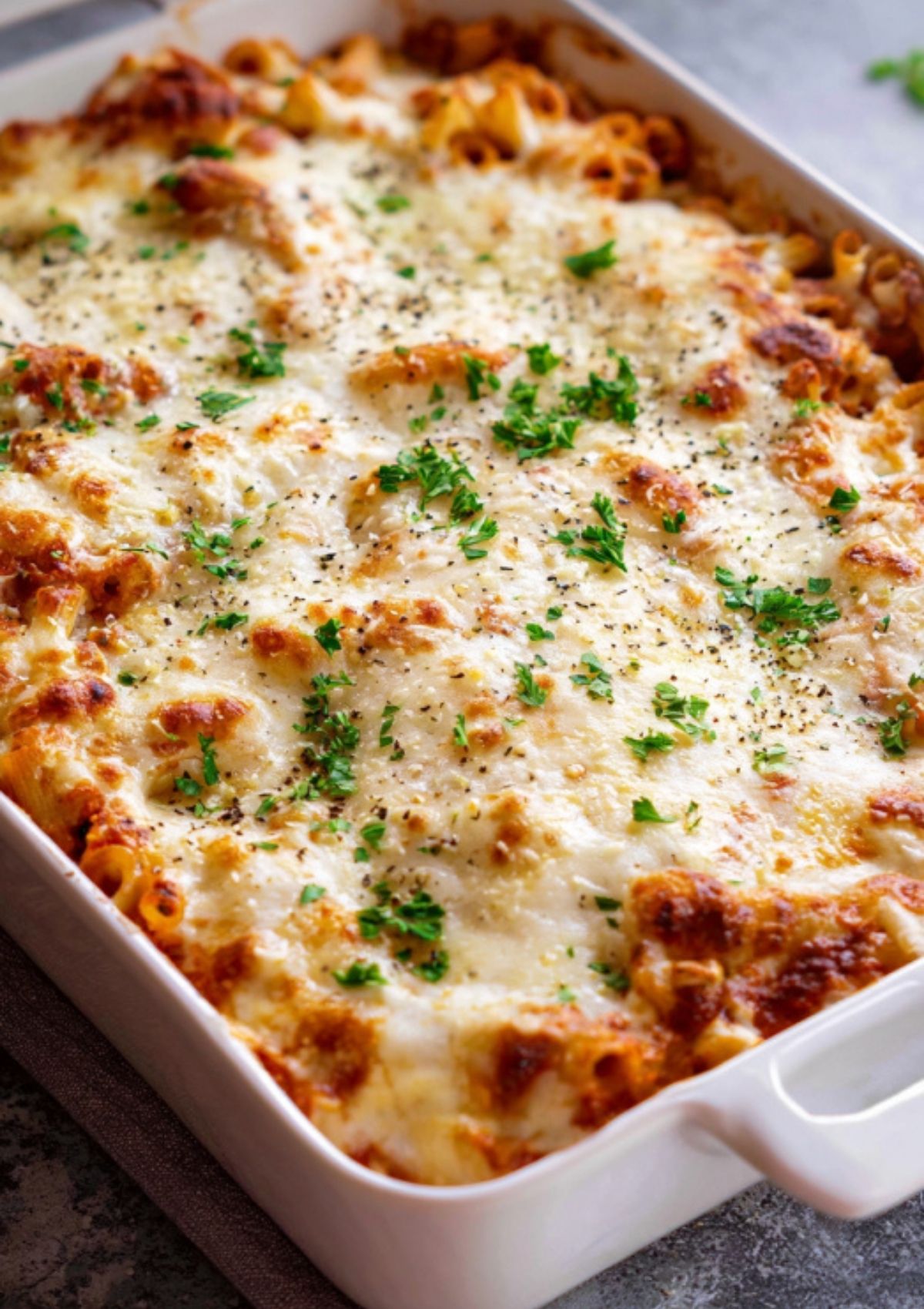 Golden baked ziti topped with melted cheese and fresh herbs in a white casserole dish.