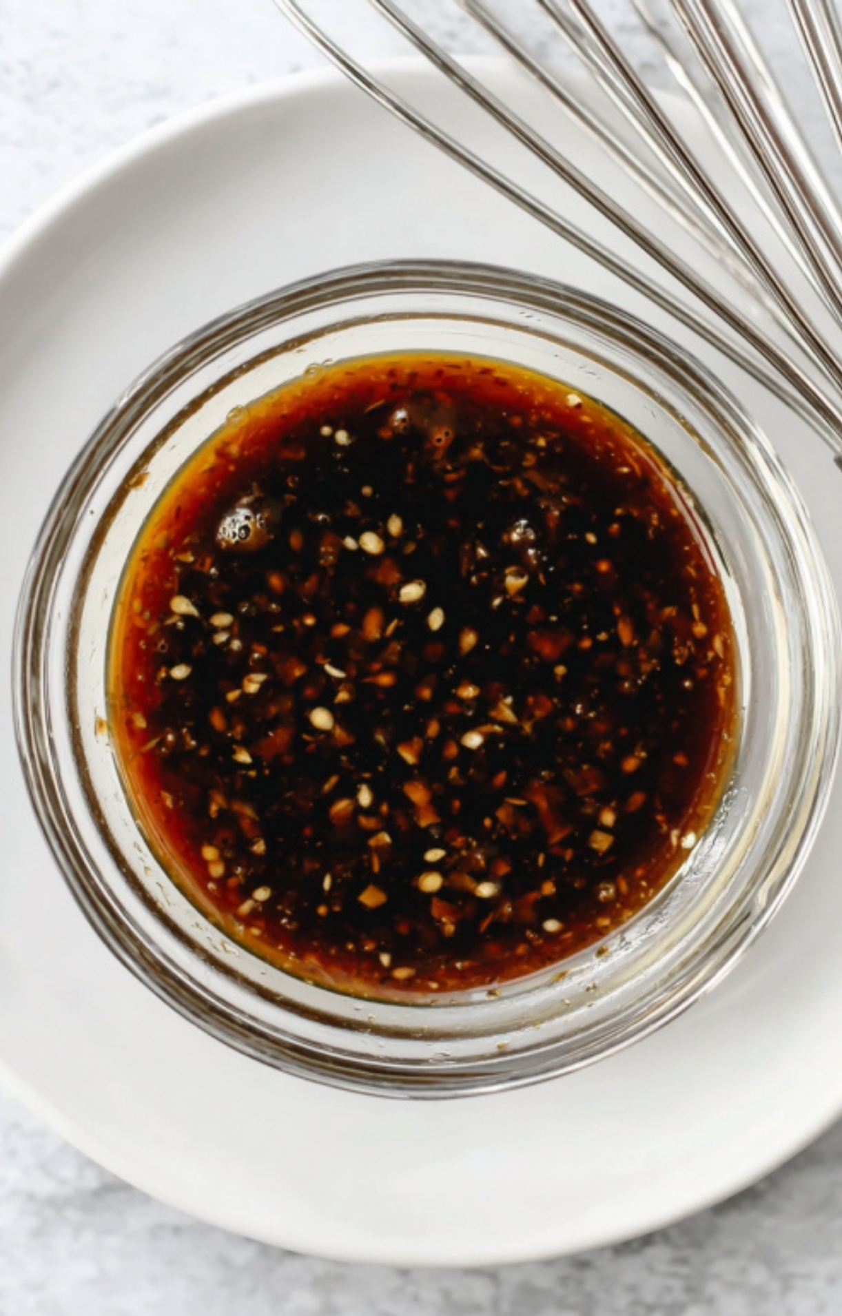 Overhead shot of homemade maple-soy glaze in a small glass jar, showing flecks of sesame seeds and fresh ginger.