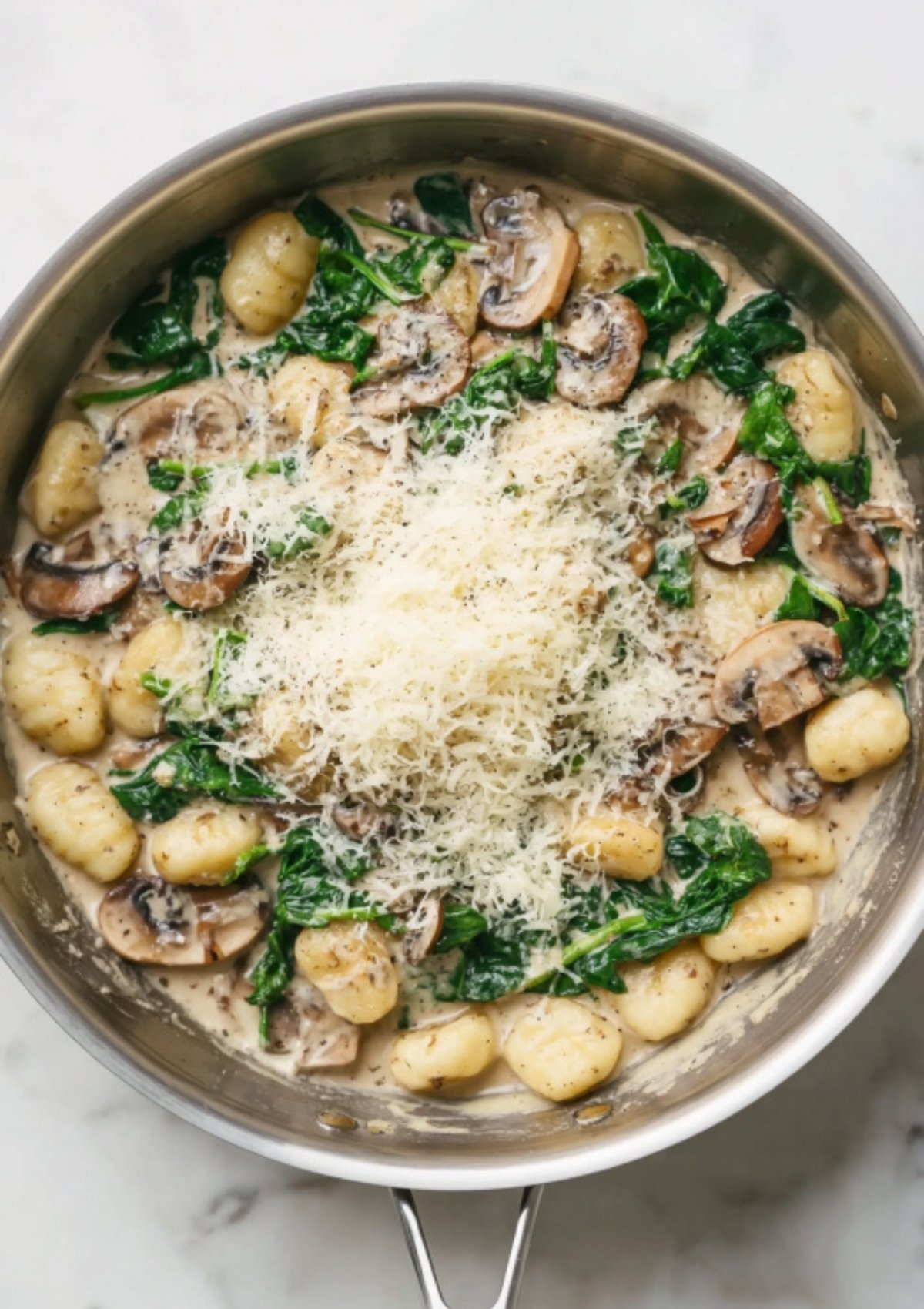 Gnocchi and mushrooms in a creamy sauce, topped with a generous pile of shredded Parmesan cheese and fresh spinach. Ideal for fall and winter dinners.