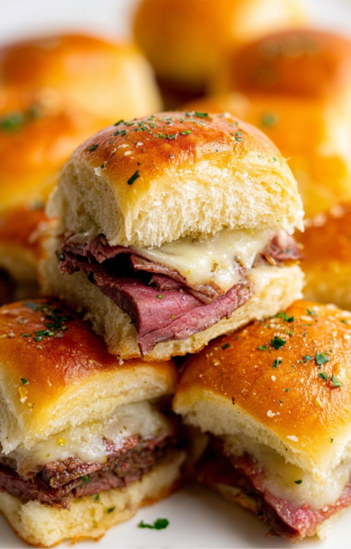 Close-up of roast beef sliders with melted provolone cheese on golden dinner rolls, topped with garlic butter and herbs, perfect for parties or family gatherings.