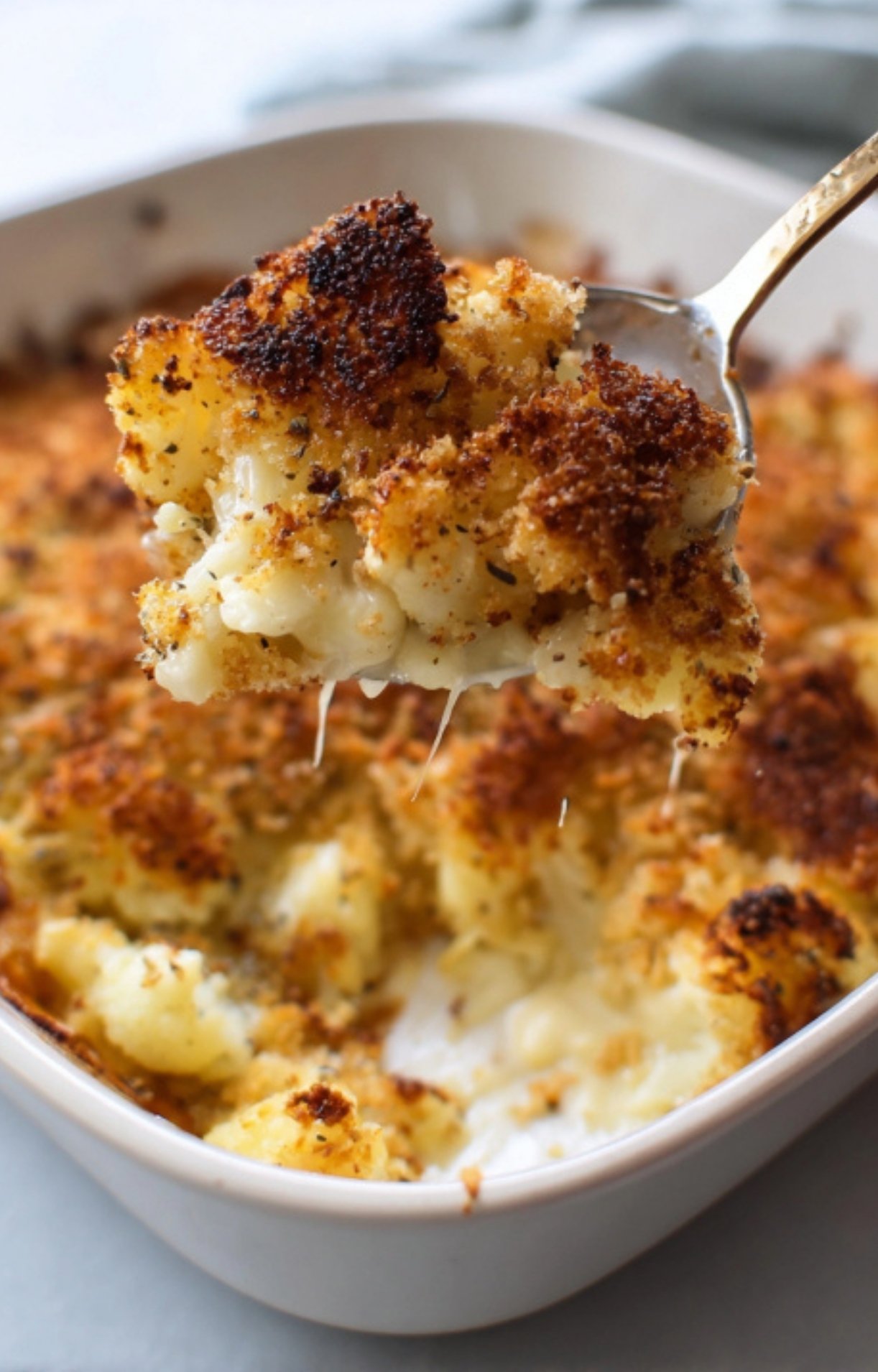 Spoonful of bubbly, golden cauliflower cheese gratin lifted from a baking dish, a classic creamy side for Sunday roast.