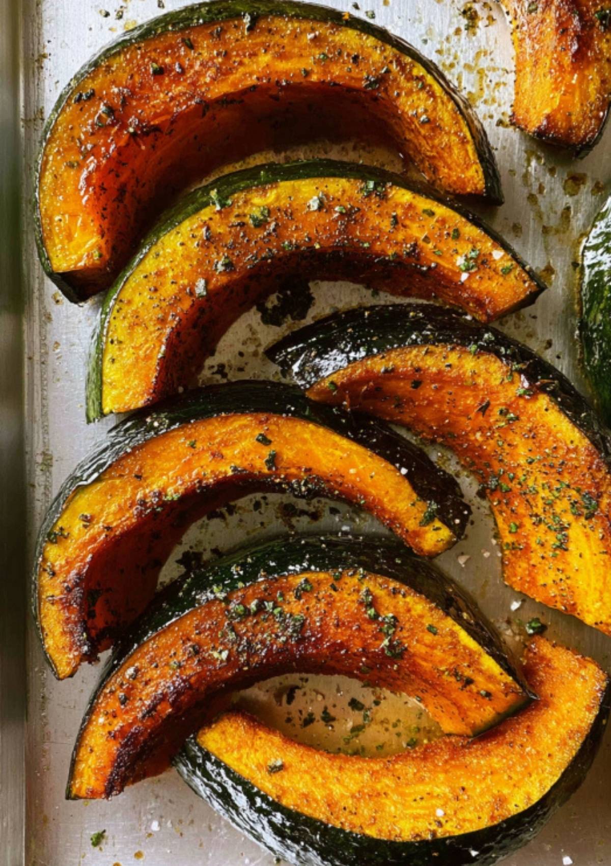 Deeply caramelized kabocha pumpkin wedges on a baking tray, golden brown edges and speckled with seasoning.