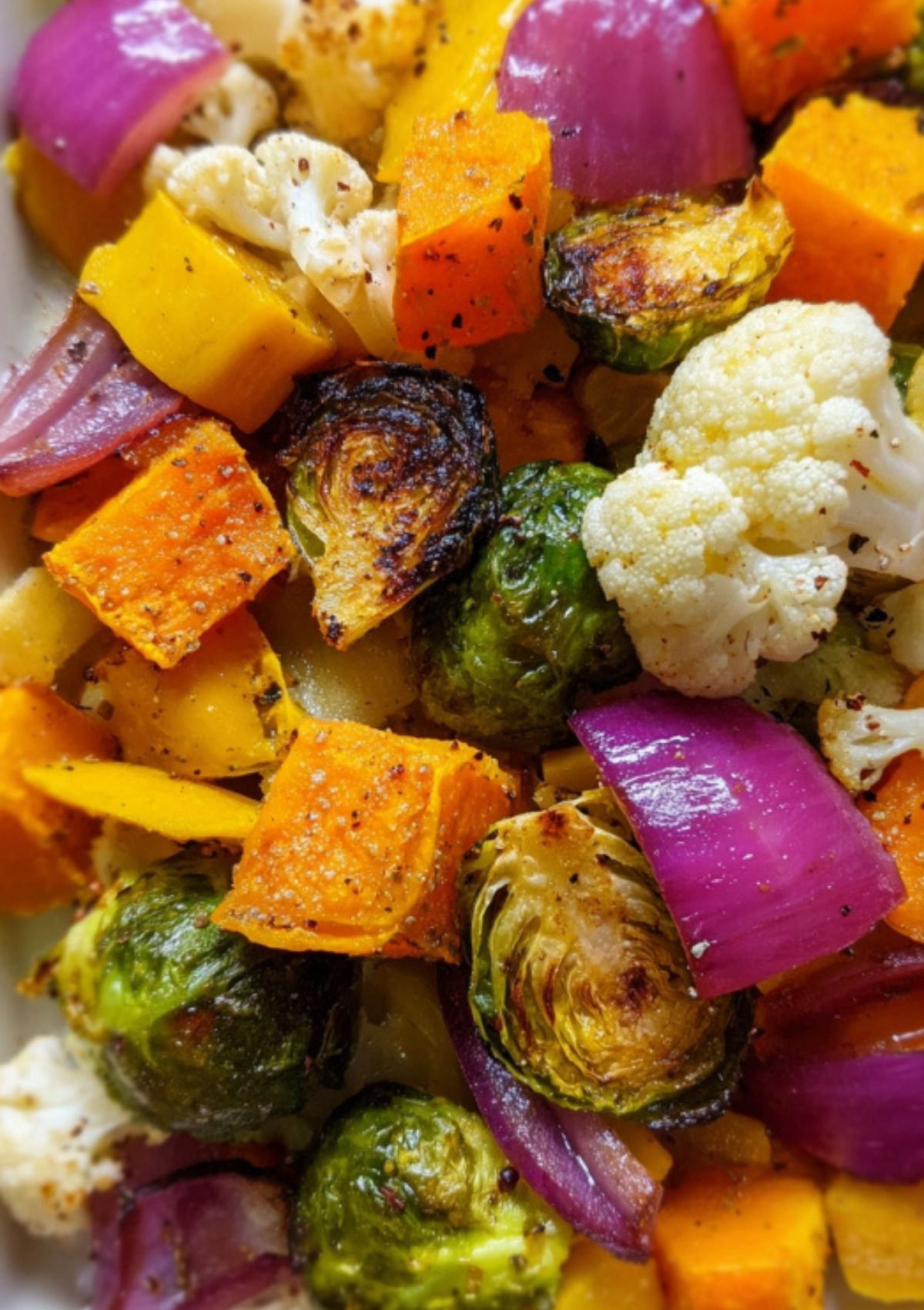 Closeup of roasted butternut squash, brussels sprouts, cauliflower, and red onion with golden, caramelized edges.