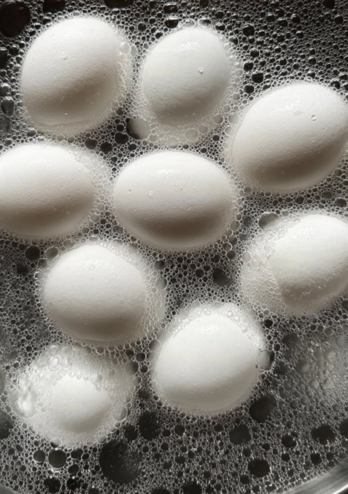 White eggs boiling in water with bubbles, the first step for making soy marinated hard boiled eggs.
