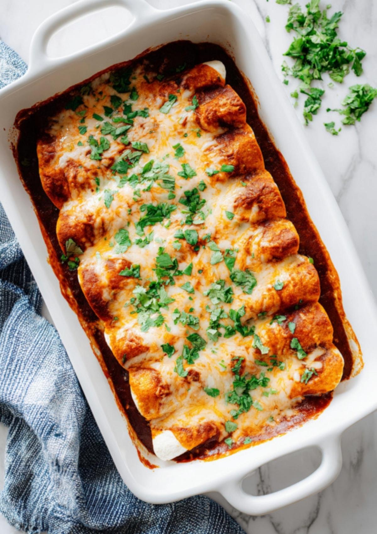 Casserole dish filled with baked black bean enchiladas topped with melted cheese and fresh cilantro. Easy vegetarian dinner perfect for family meals.