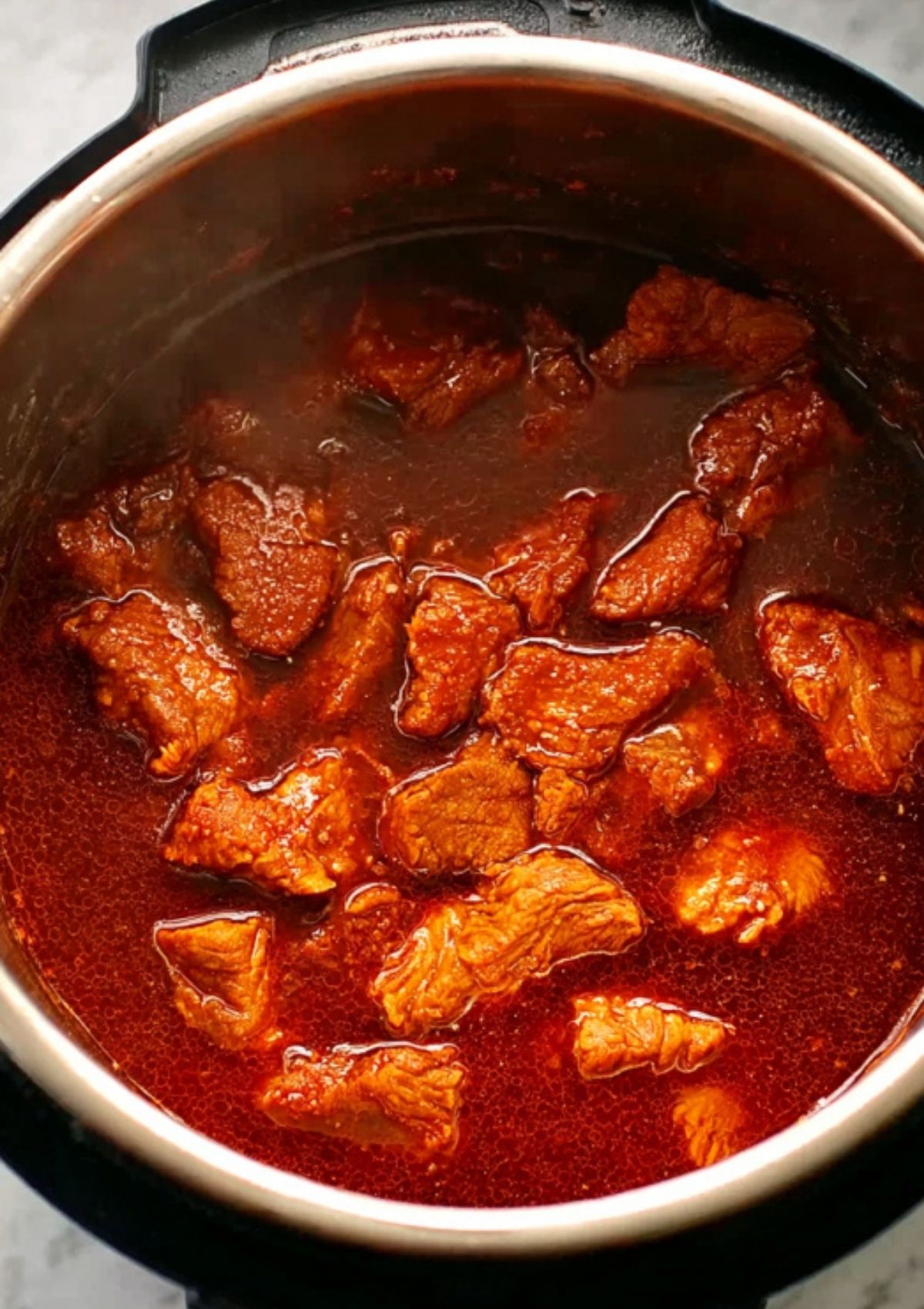 Chunks of pork simmering in rich barbecue sauce in an Instant Pot, ready for shredding.