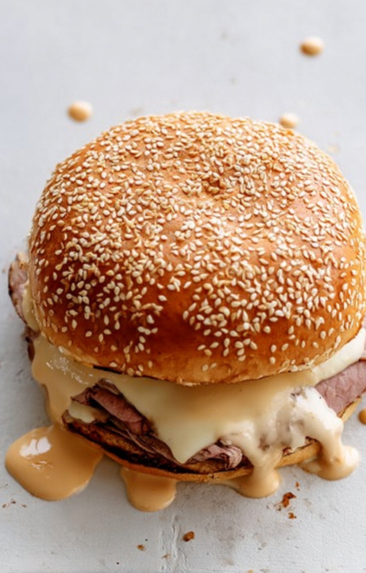 Sesame seed bun filled with thinly sliced roast beef and creamy cheddar cheese sauce, dripping down the sides