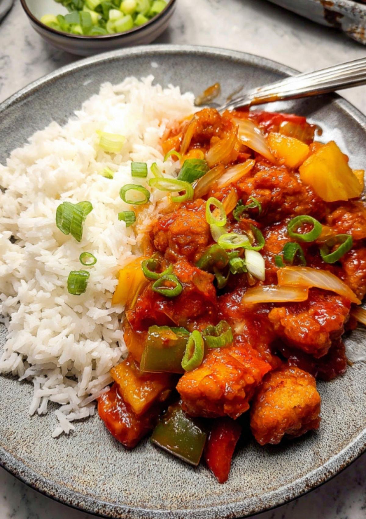 Sweet and sour pork with pineapple, bell peppers, and onions served with steamed white rice in a bowl.
