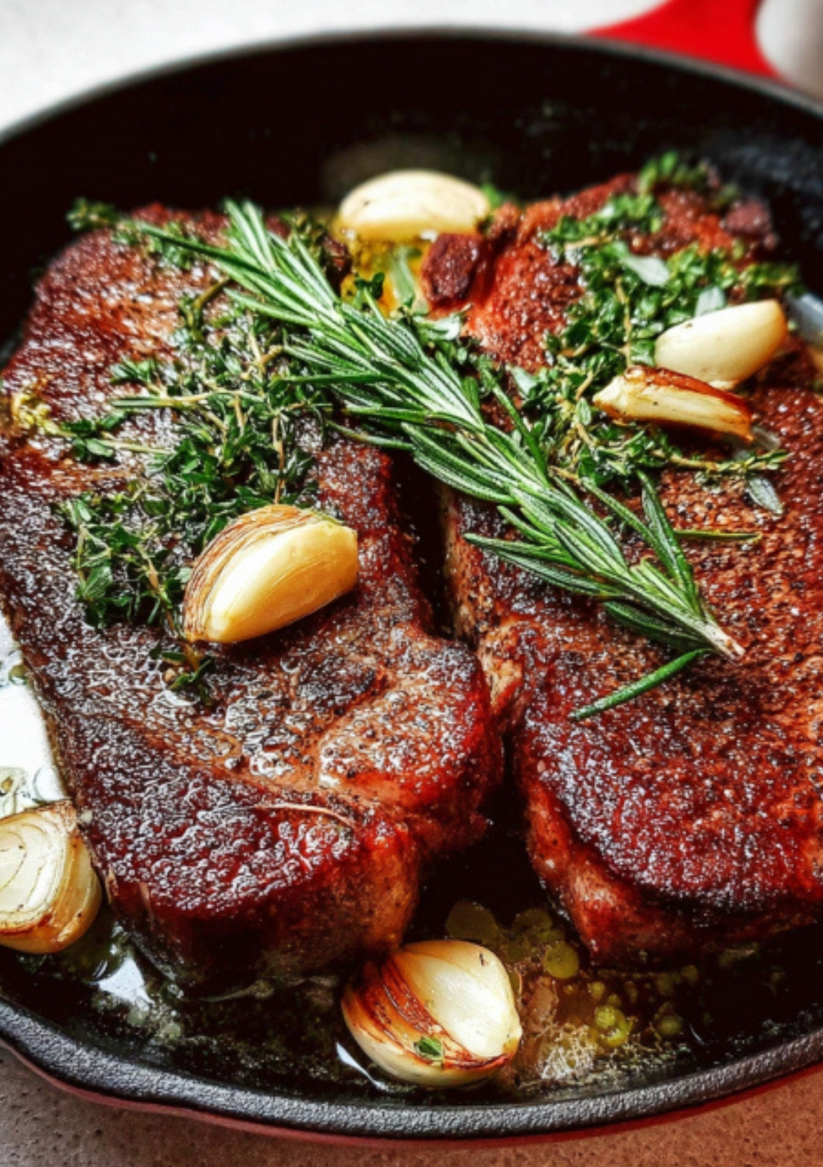 Two seared steaks in a cast iron skillet with rosemary, thyme, and whole garlic cloves. Juicy pan seared steak perfect for easy steak night and restaurant style dinners.