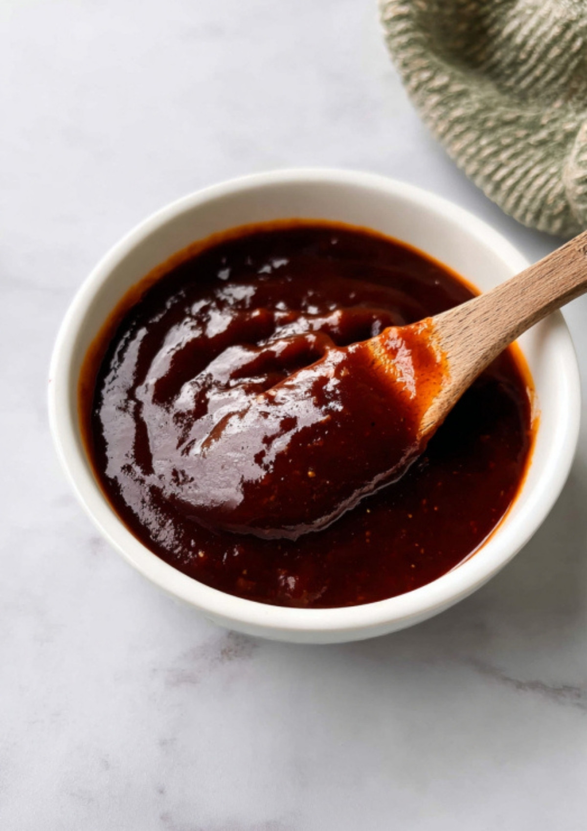Small white bowl of katsu sauce with a wooden spoon on a marble countertop.