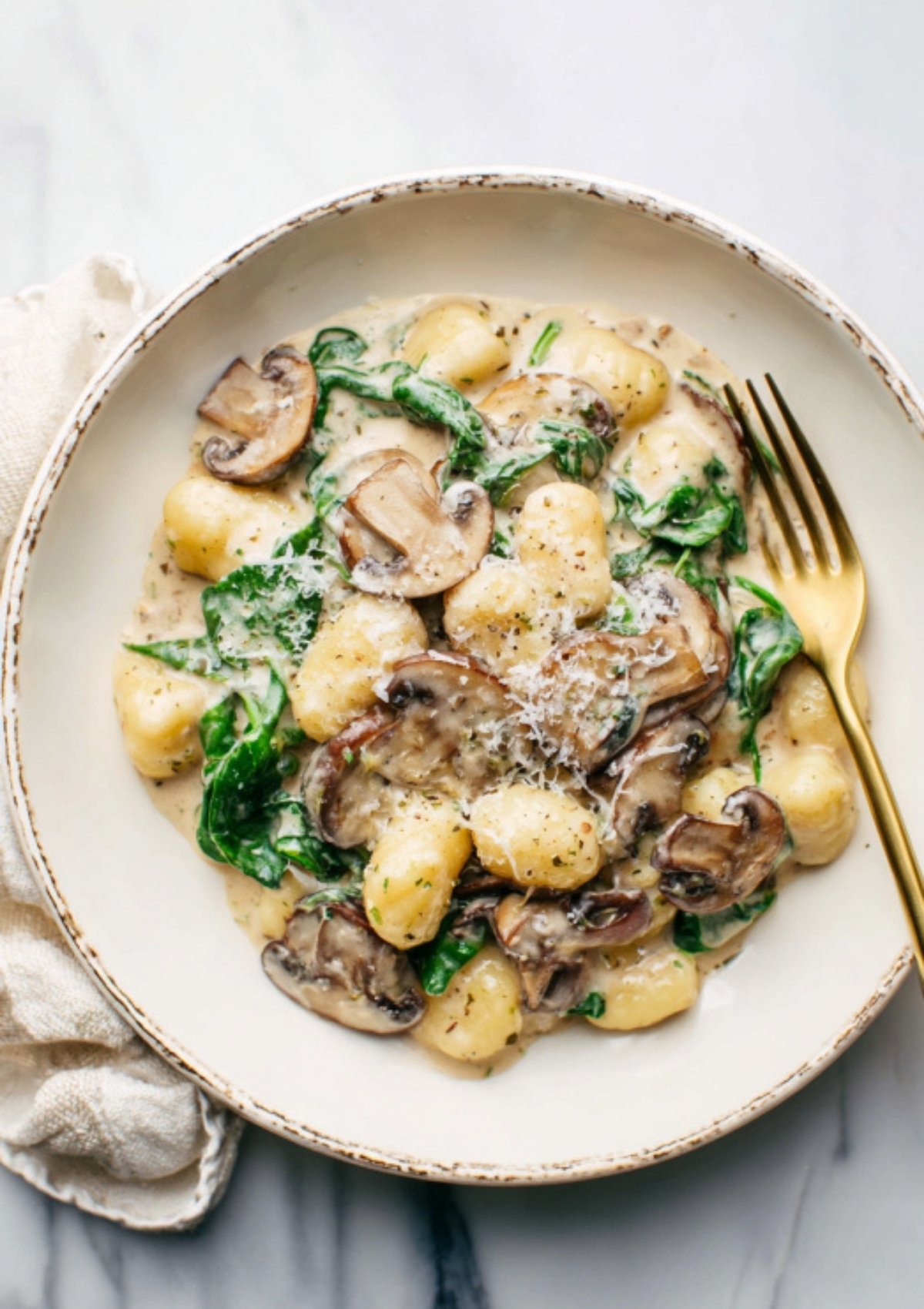 Top view of a bowl filled with creamy gnocchi, mushrooms, spinach, and Parmesan cheese. Delicious Italian-inspired comfort food.