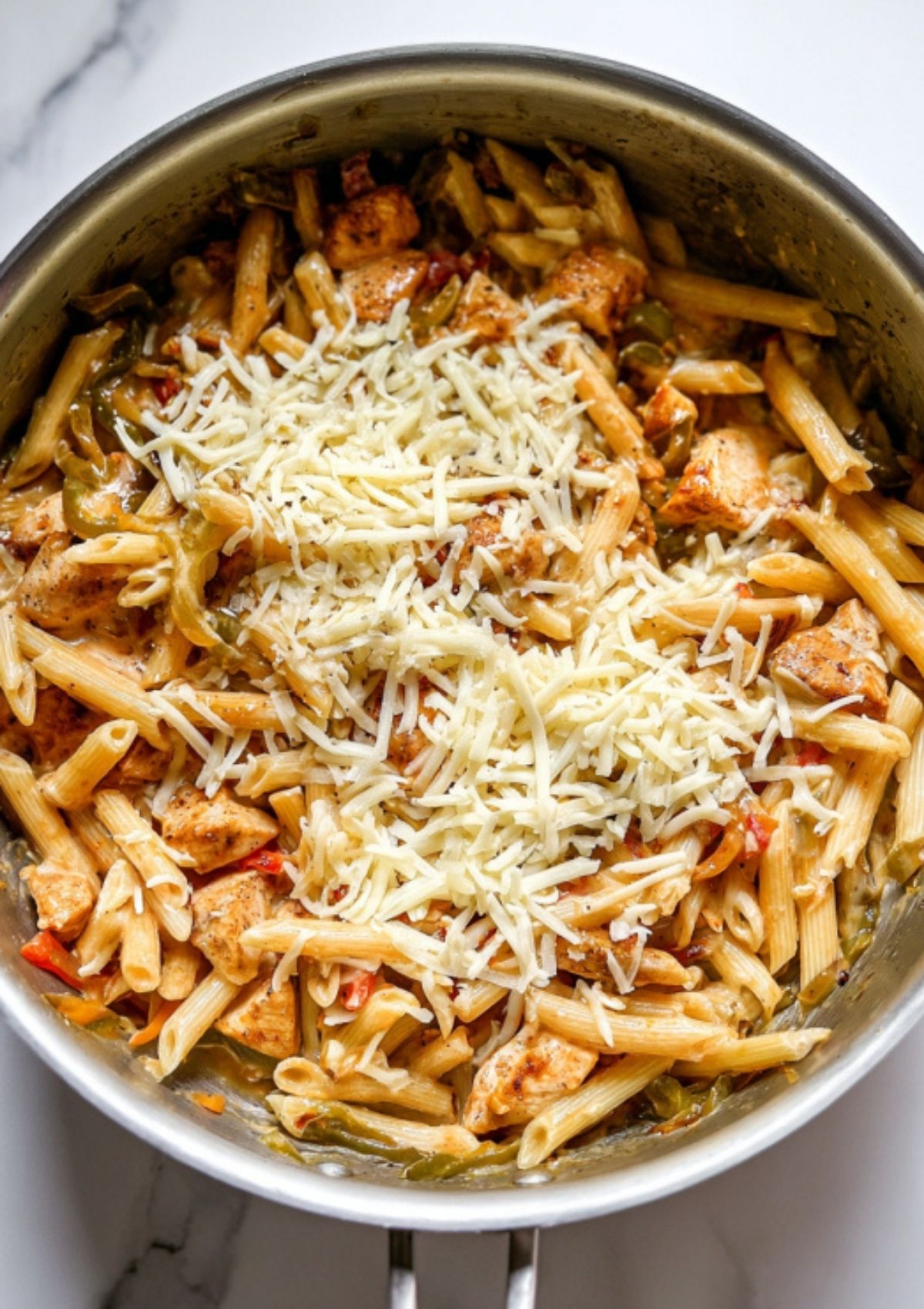 Skillet filled with penne pasta, chicken, peppers, and onions, topped with melted cheese. Perfect for easy Tex-Mex dinners and creamy pasta recipes.