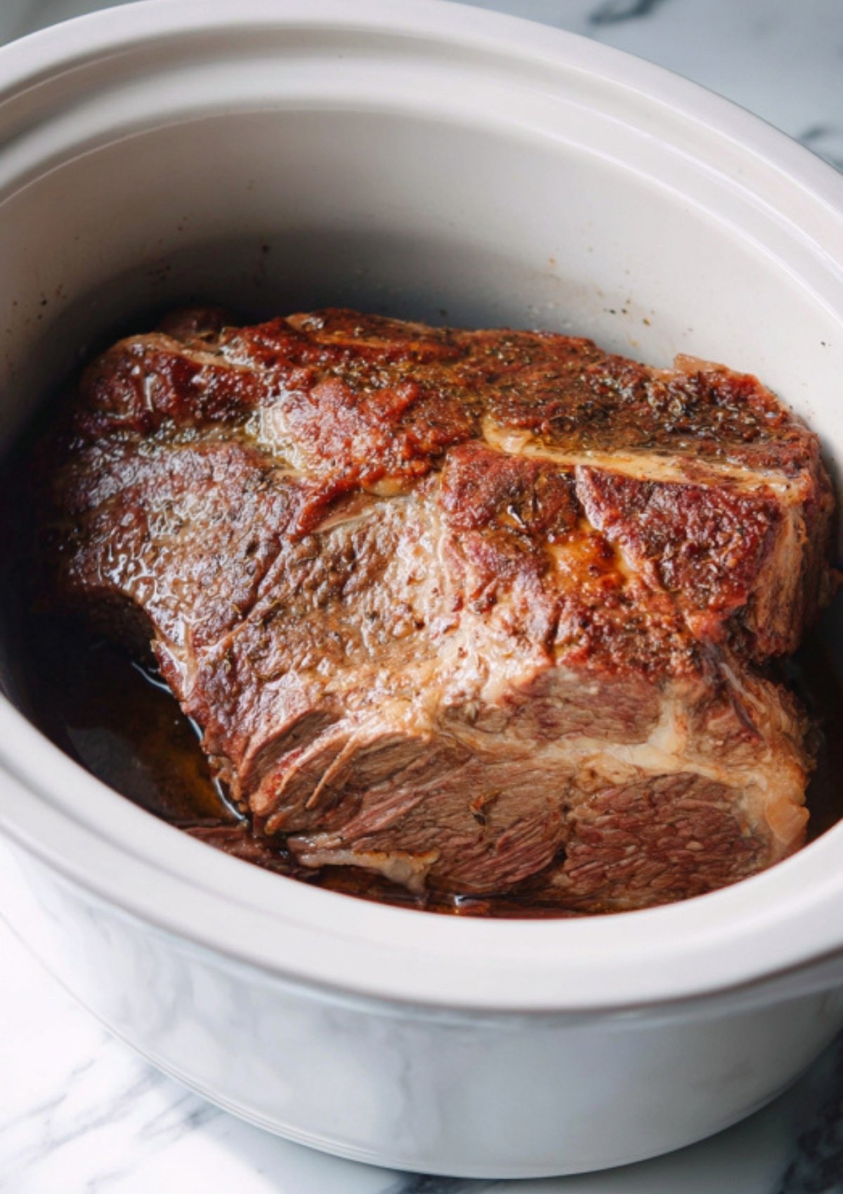 Seasoned beef chuck roast seared and ready to slow cook in a white crock pot for classic pot roast.