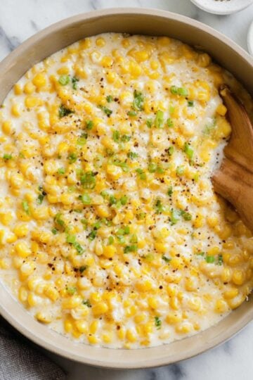 A skillet filled with creamy, cheesy canned corn and topped with chopped green onions, served hot as a classic comfort food side for family gatherings.