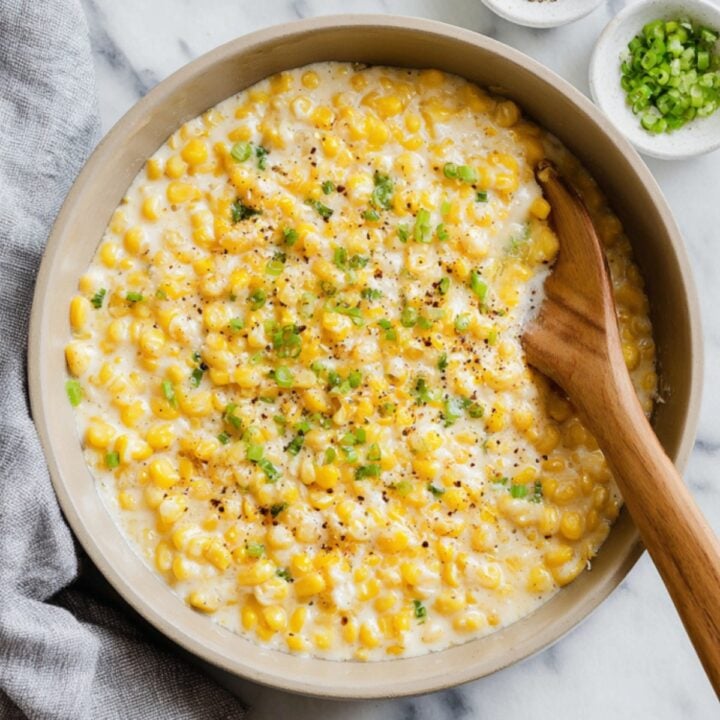 A skillet filled with creamy, cheesy canned corn and topped with chopped green onions, served hot as a classic comfort food side for family gatherings.