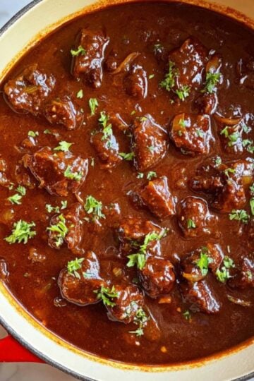 A pot filled with rich, hearty Gulasch beef goulash, topped with fresh parsley, showing a thick paprika gravy. Perfect for cozy winter dinners and easy homemade German meals.