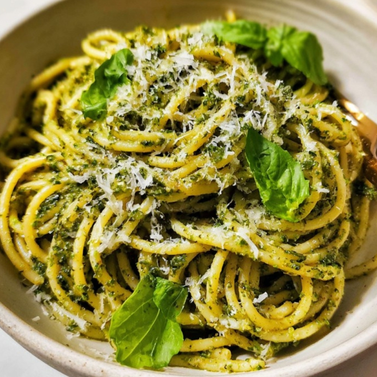 Bowl of pesto pasta topped with parmesan and basil leaves, a classic week night dinner idea, featuring easy, homemade Italian flavors and vegetarian comfort.