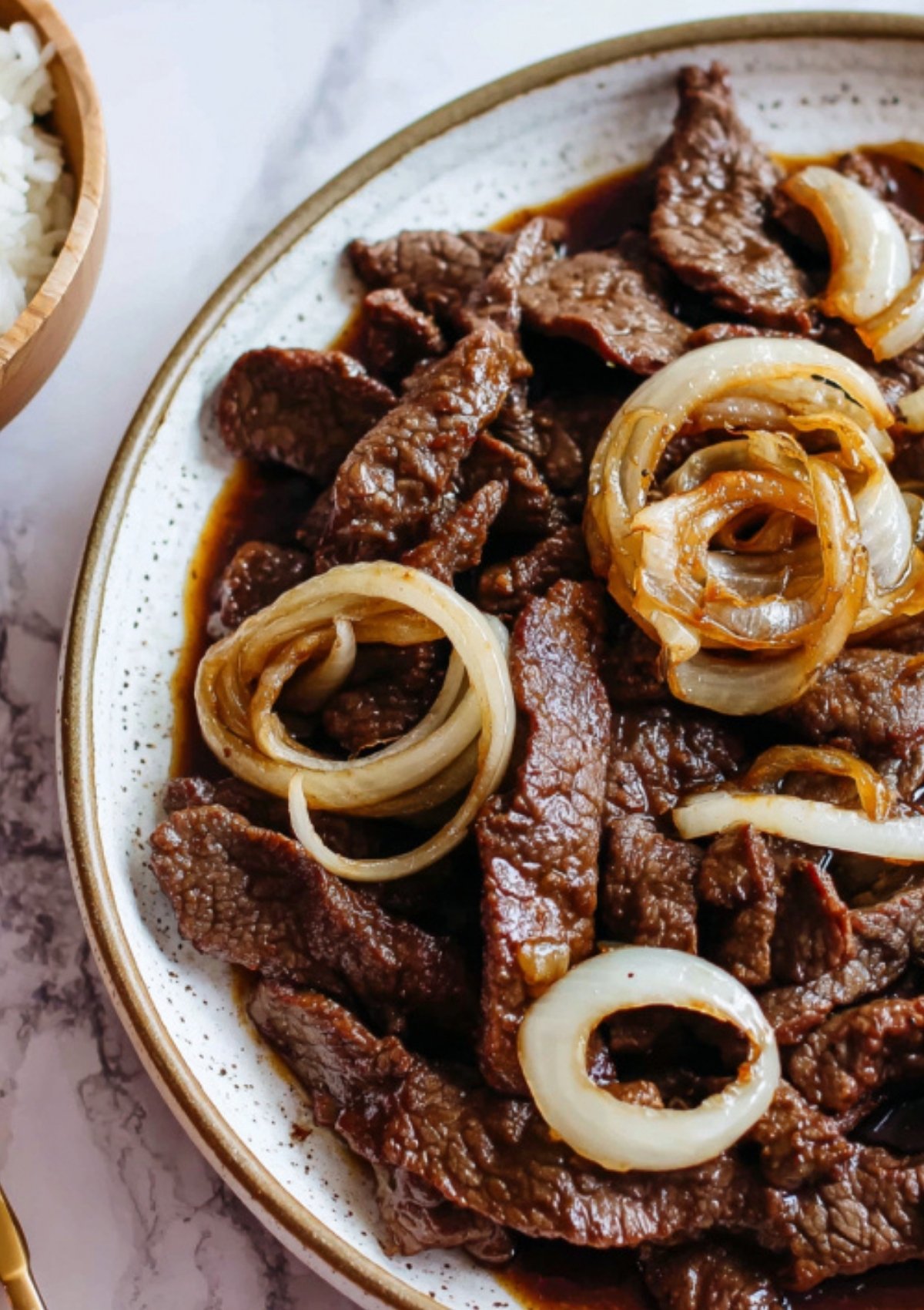 Close up of Beef Steak Filipino with soft onion rings in a rich soy citrus sauce on a plate.