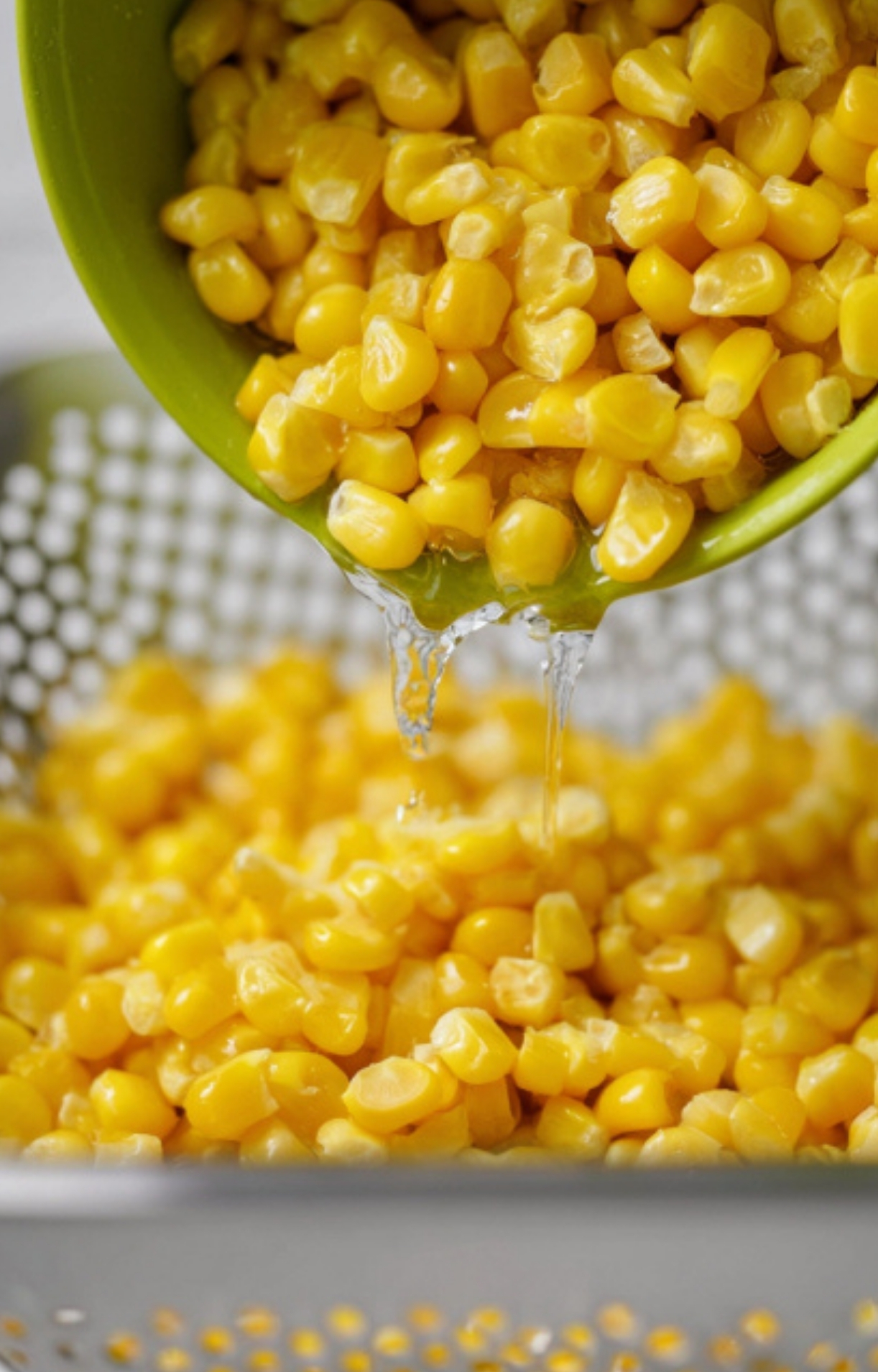 Draining canned corn in a green colander, the first step for making homemade creamy canned corn, perfect for fast holiday cooking or easy weeknight dinners.