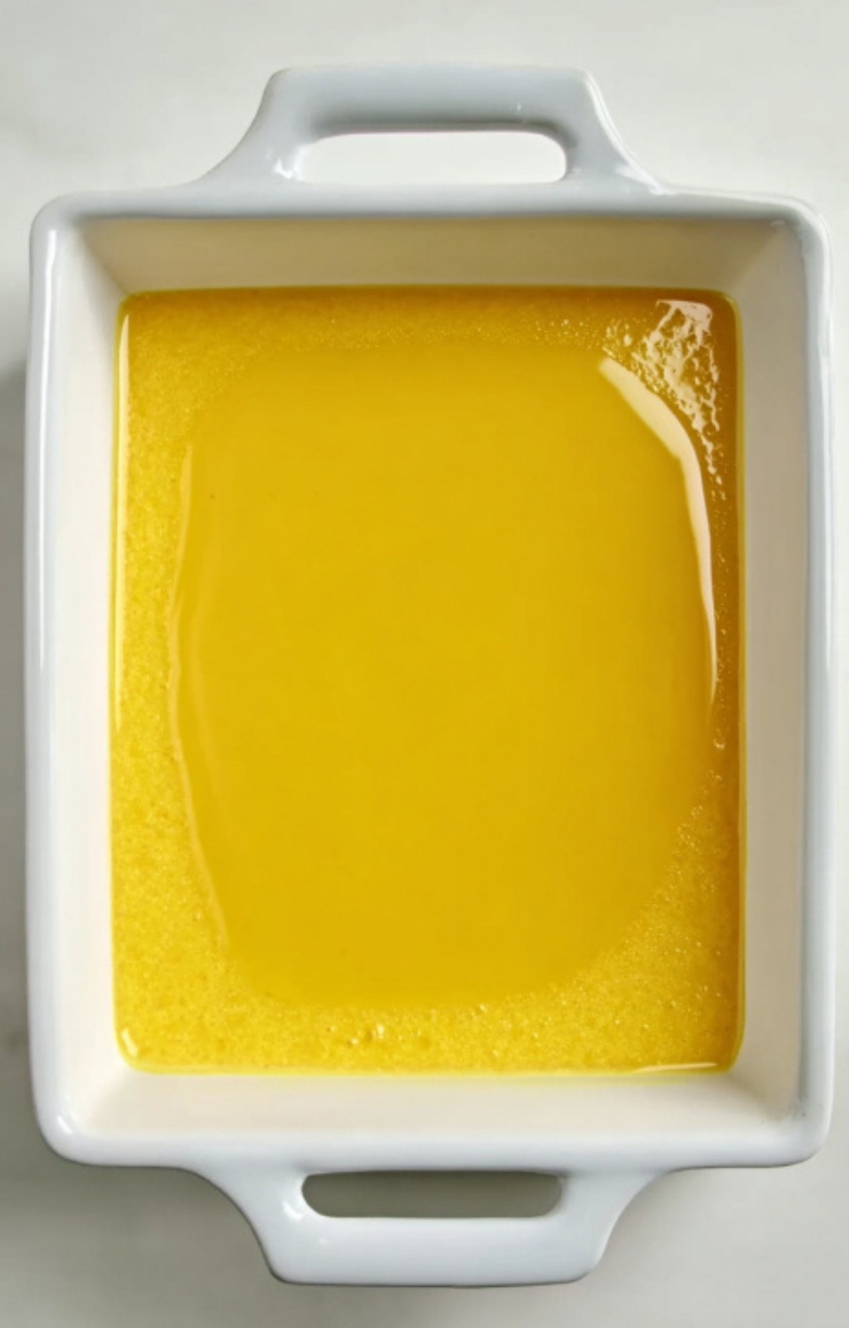 Melted butter in a casserole dish, the first step for making easy corn pudding casserole. Classic Southern comfort food for potlucks and holidays.