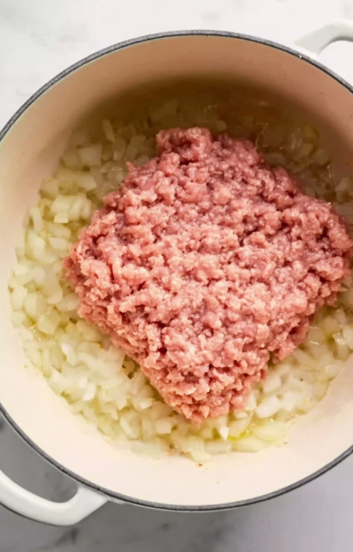 Uncooked ground meat and diced onions in a Dutch oven, the first step for homemade cheesy goulash. Classic recipe prep for hearty pasta casseroles and comfort food favorites.