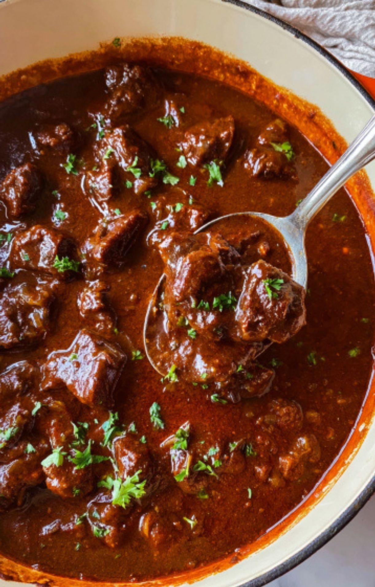 A spoonful of beef goulash lifted from a Dutch oven, showing chunks of tender beef in a thick, flavorful sauce. Ideal for easy homemade dinners and German cuisine lovers.