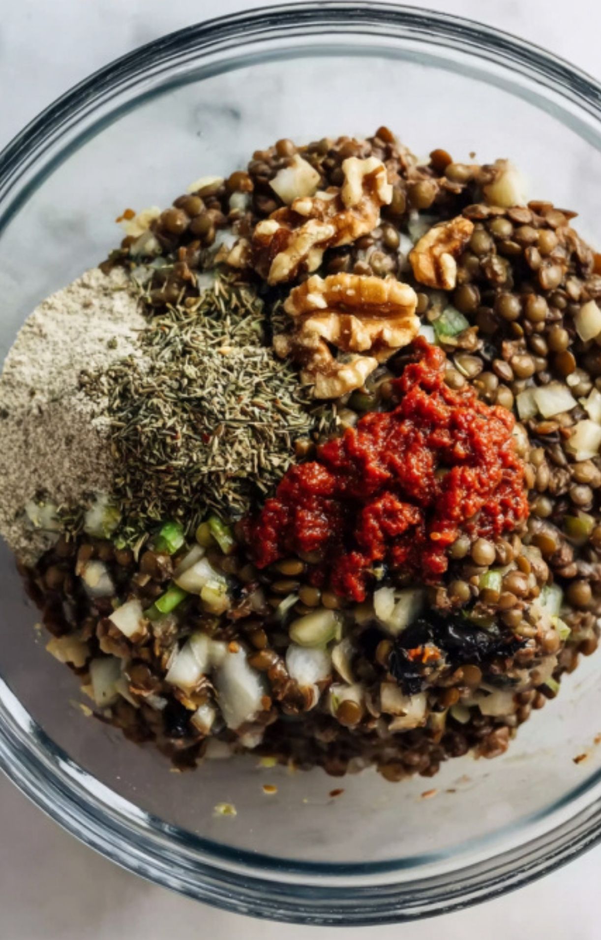 A glass bowl filled with cooked lentils, chopped walnuts, onion, spices, and tomato paste for a flavorful vegan wellington filling.