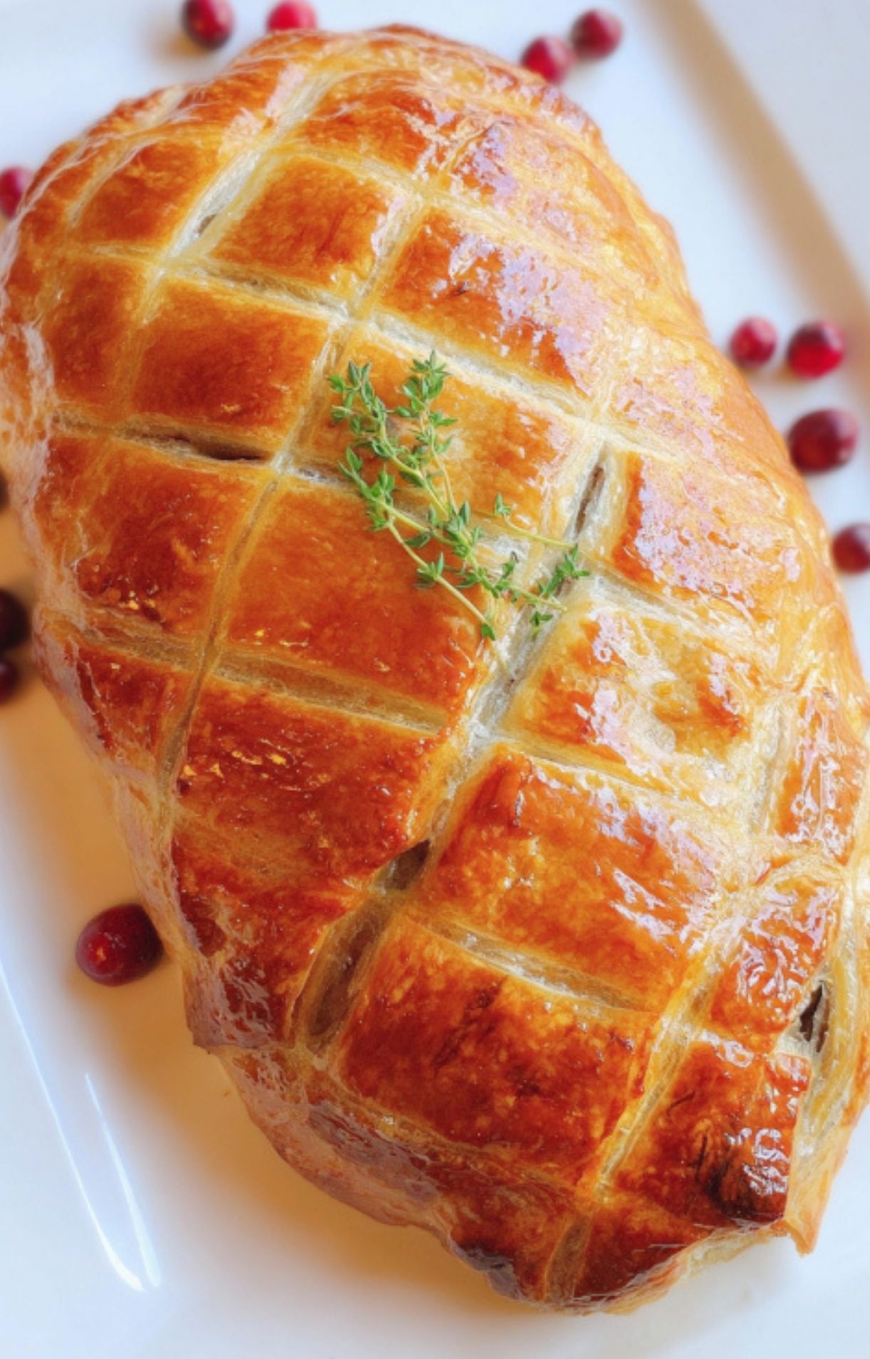 Whole Christmas Beef Wellington with golden puff pastry, garnished with fresh thyme and cranberries. Beautiful centerpiece for Christmas celebrations.