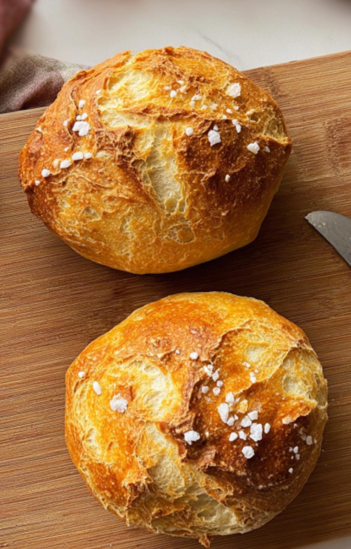 Two homemade golden dinner rolls with a crispy crust, topped with flaky sea salt, served as a side for beef Wellington.
