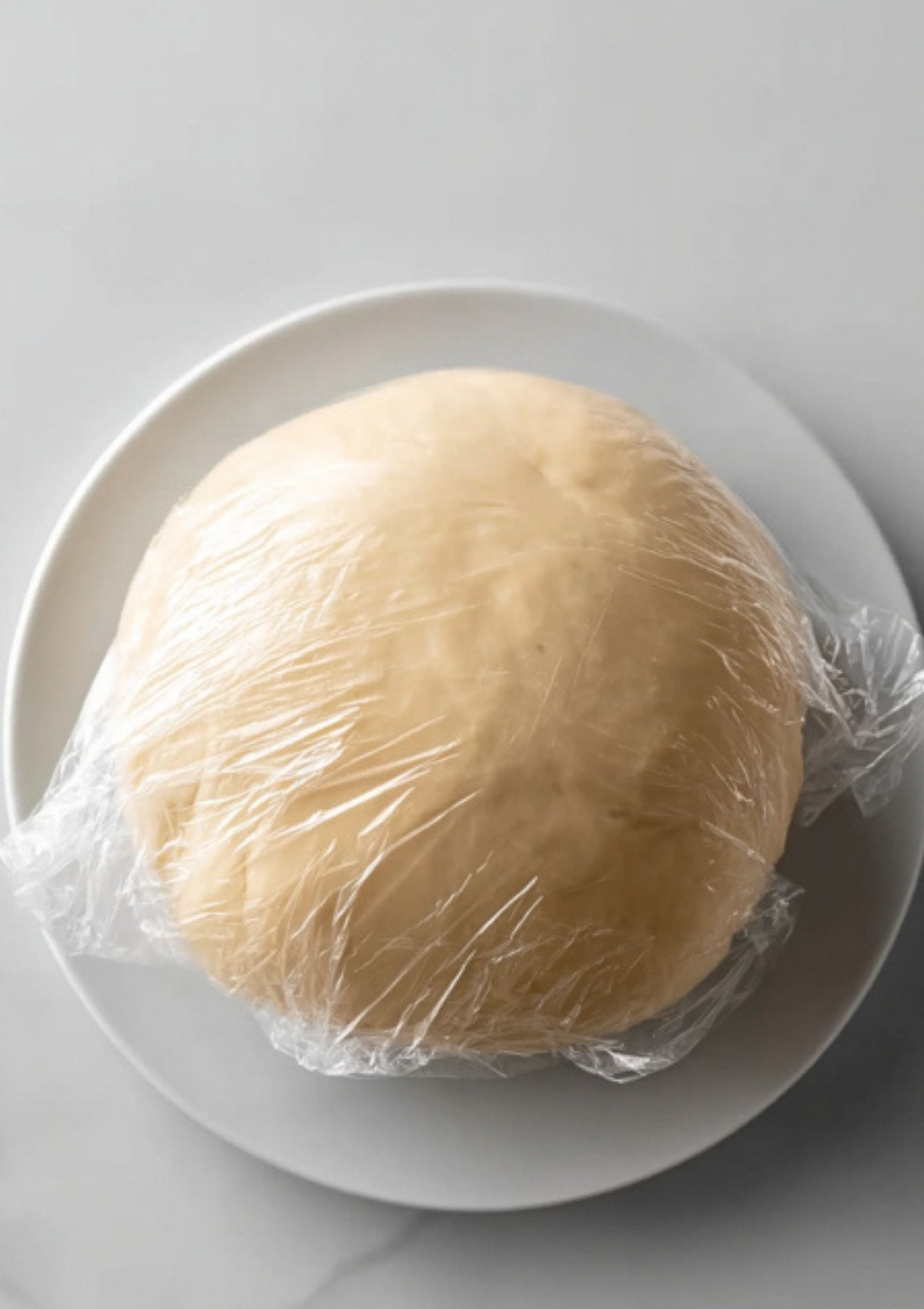 Ball of gluten free pastry dough wrapped in plastic wrap, chilling before rolling for a crisp and golden beef wellington crust.