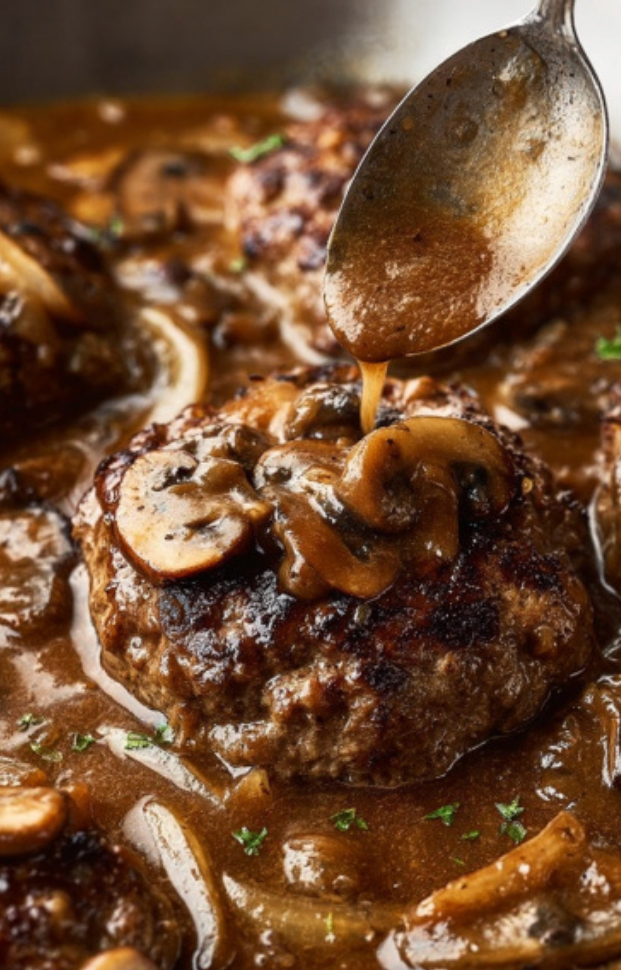 Spoon drizzling rich mushroom gravy over Salsberry Steak patties in skillet—a delicious, hearty dinner recipe for meat lovers and fans of classic home-cooked meals.