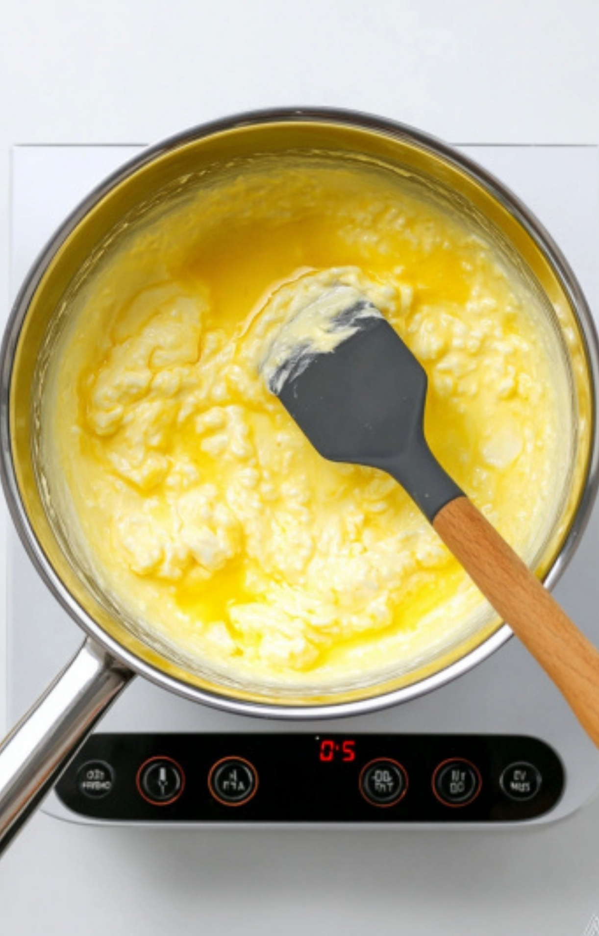 Cream cheese and melted butter being stirred together in a saucepan, the first step for making creamy corn casserole.