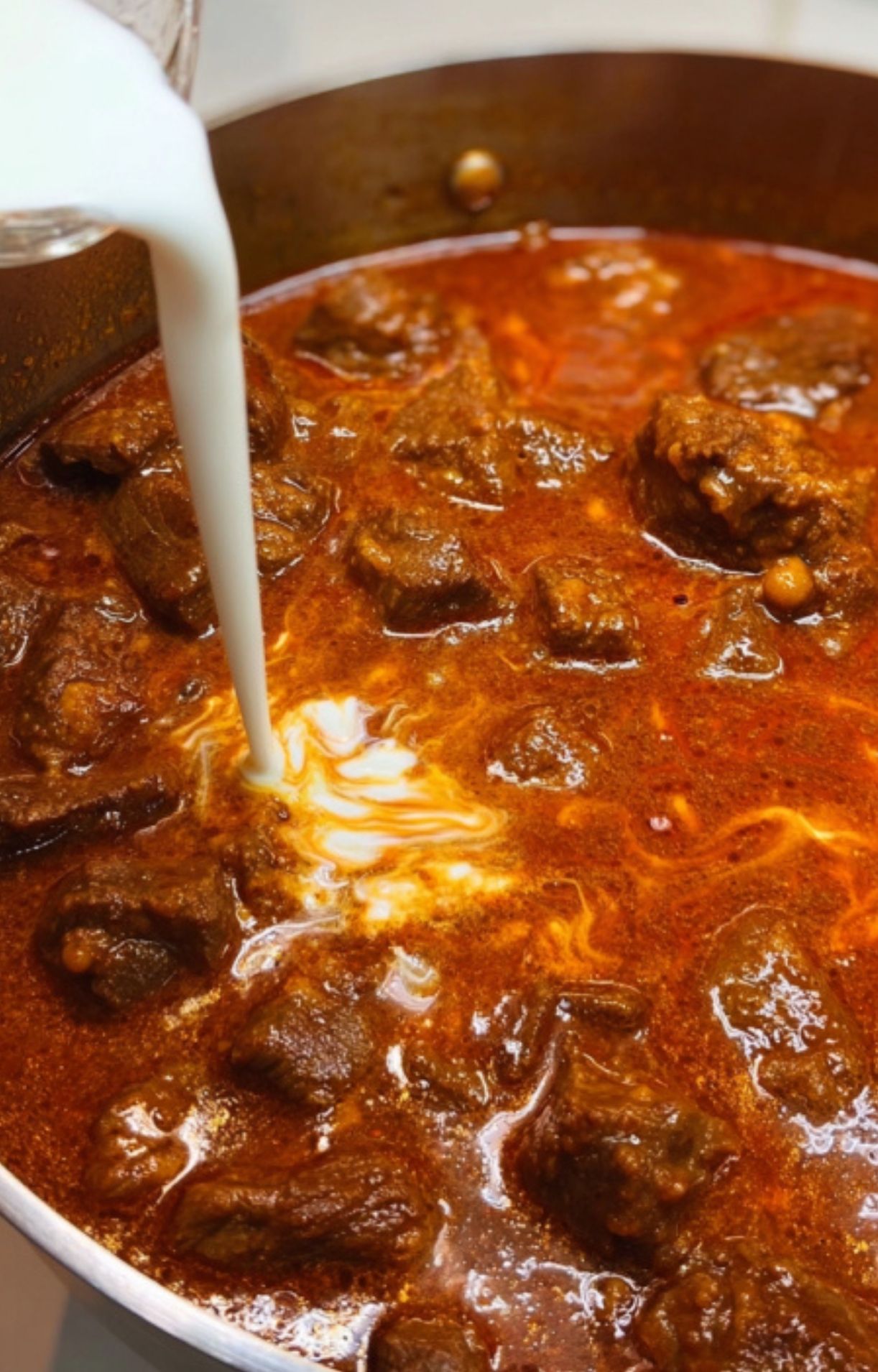 Cream being swirled into simmering beef goulash for a silky, rich finish. Perfect for hearty winter dinners and traditional German recipes.