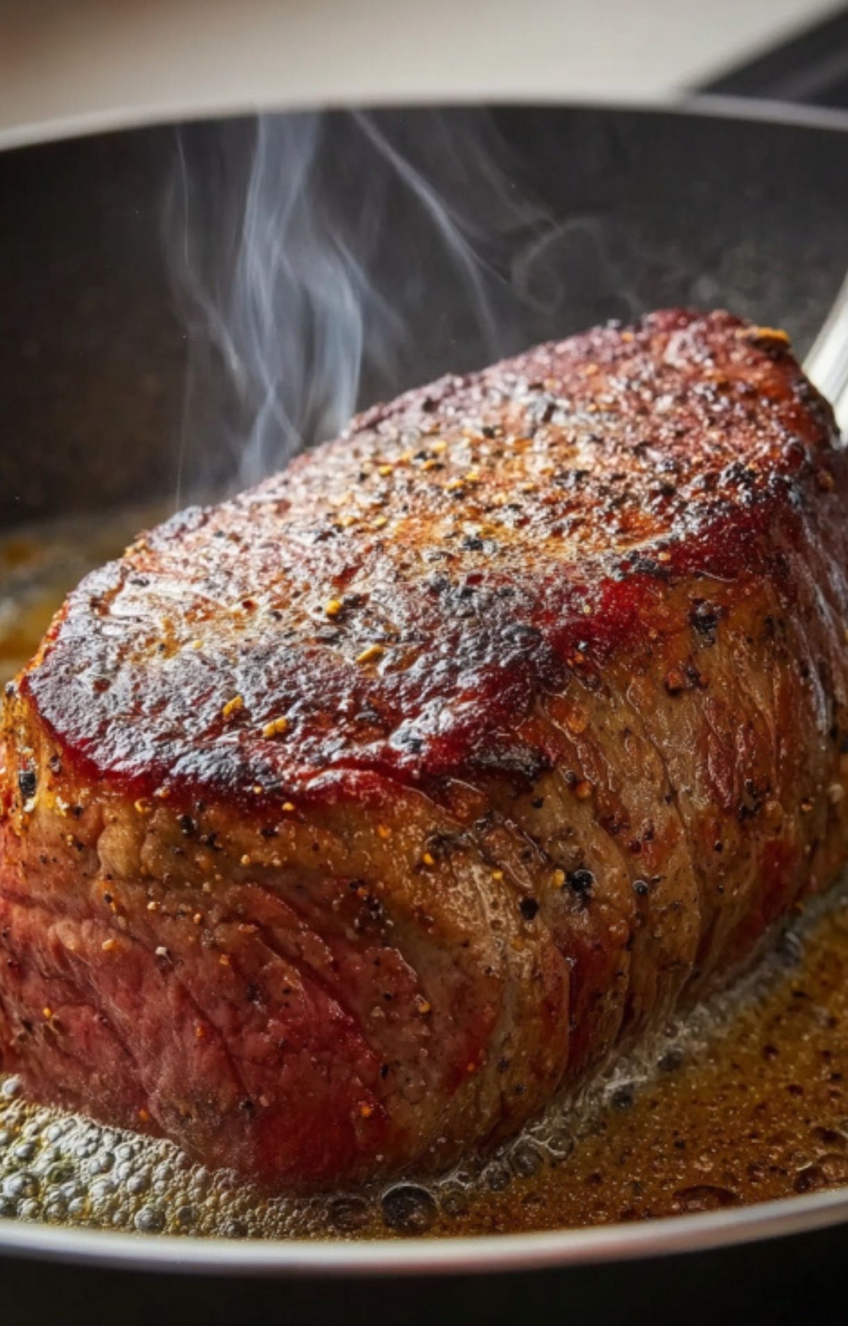 Beef tenderloin sizzling in a hot pan, perfectly seared with pepper and salt, step one for Christmas Beef Wellington. Holiday dinner prep made easy.
