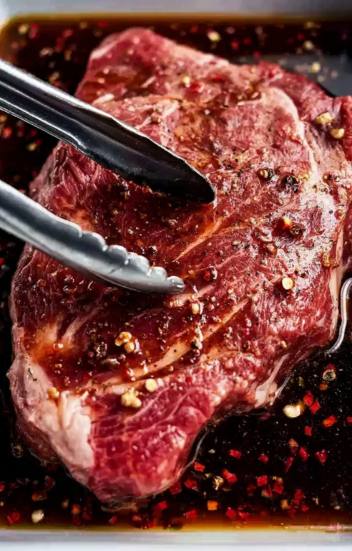Chuck steak soaking in rich marinade, being turned with tongs, perfect for meal prep and grilling season