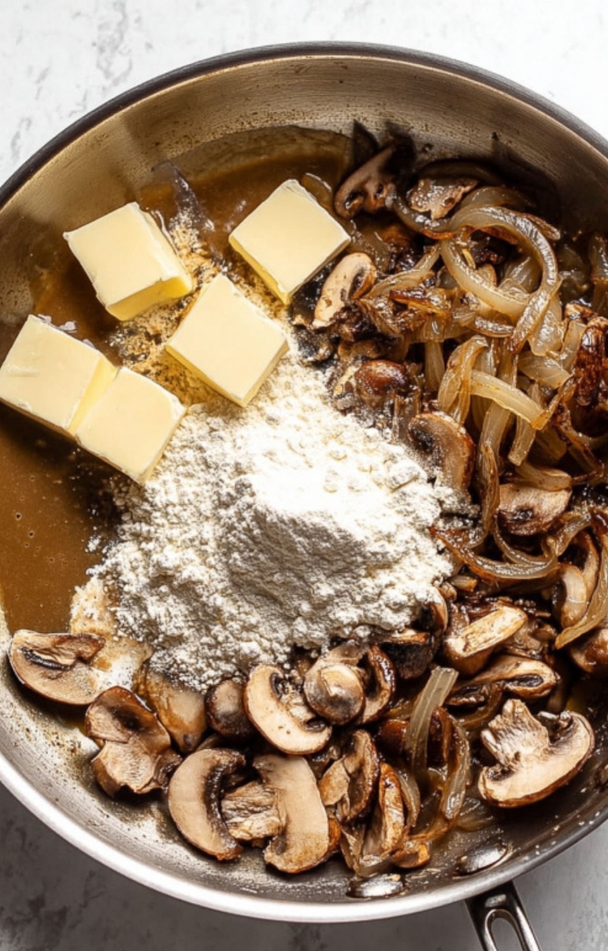 Butter and flour added to sautéed onions and mushrooms in a skillet, the base for rich homemade mushroom gravy in a classic Salsberry Steak dinner.