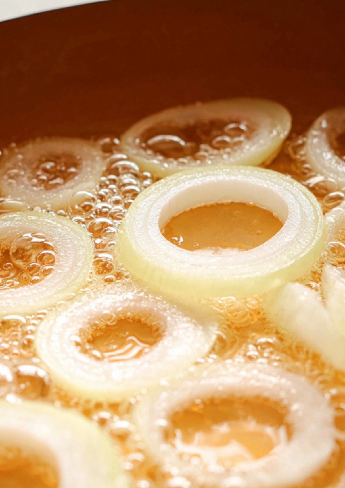 Onion rings simmering in hot oil until soft and golden for Beef Steak Filipino.